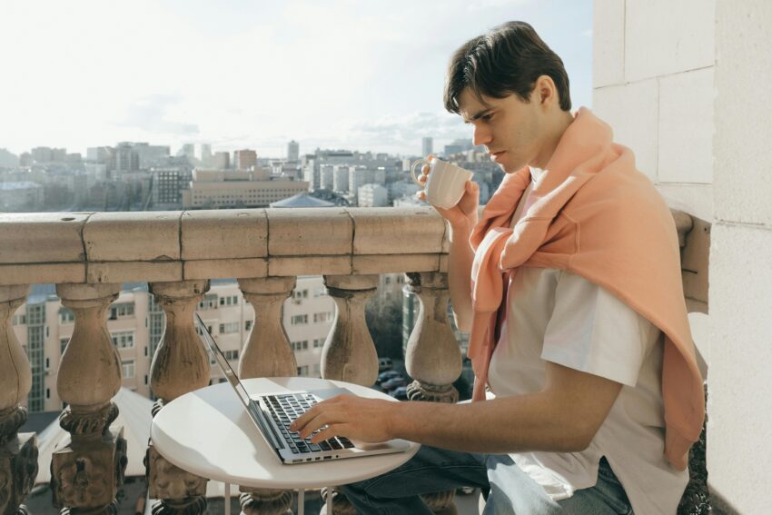 mężczyzna siedzi na balkonie i pracuje na swoim laptopie
